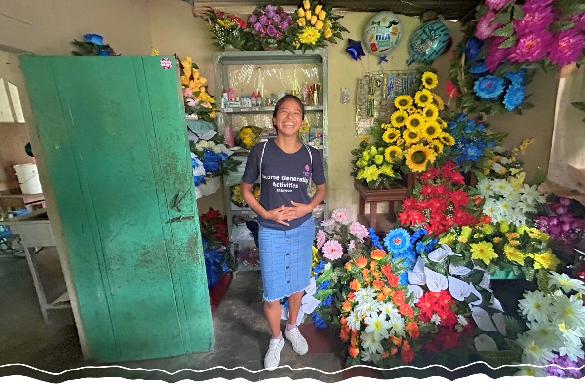 a woman is grinning, standing in a room surrounded by flowers